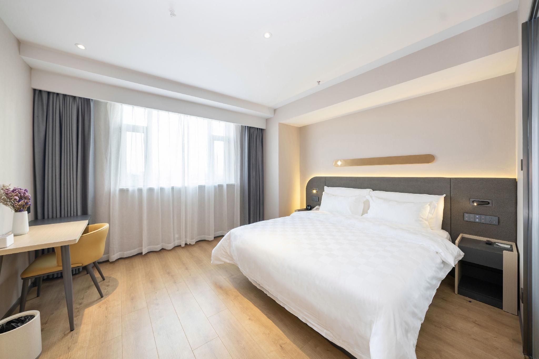 A hotel room with a bed, a desk, a chair, and a window with curtains.