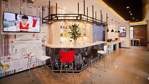 A modern bar area with a curved counter, bar stools, and a television screen displaying a sports event. - Ibis Harbin Hongqi Street Hotel (Harbin)