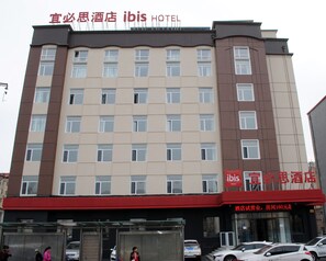 A hotel building with multiple floors, large windows, and a red awning. - Ibis Harbin Hongqi Street Hotel (Harbin)