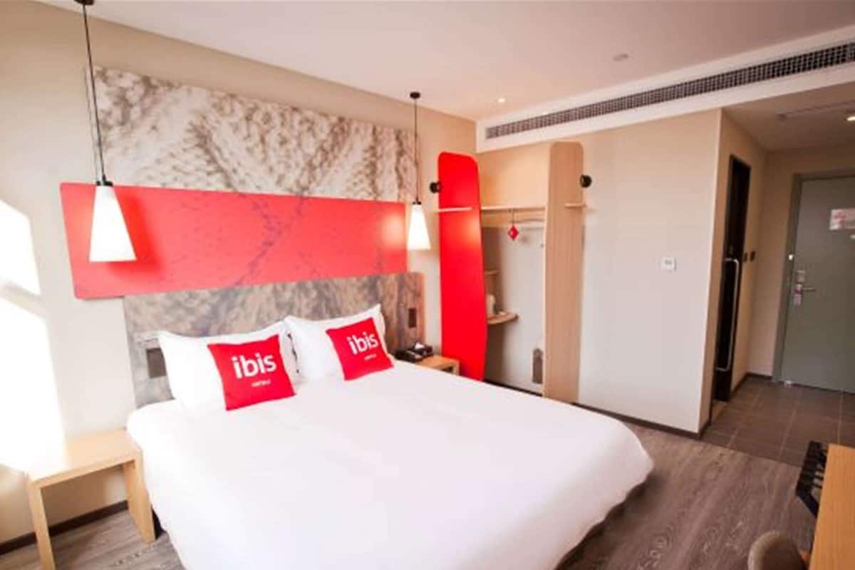 Ein Hotelzimmer mit einem Bett, einer roten Akzentwand, einem Marmorkopfschild und einer modernen Pendelleuchte.