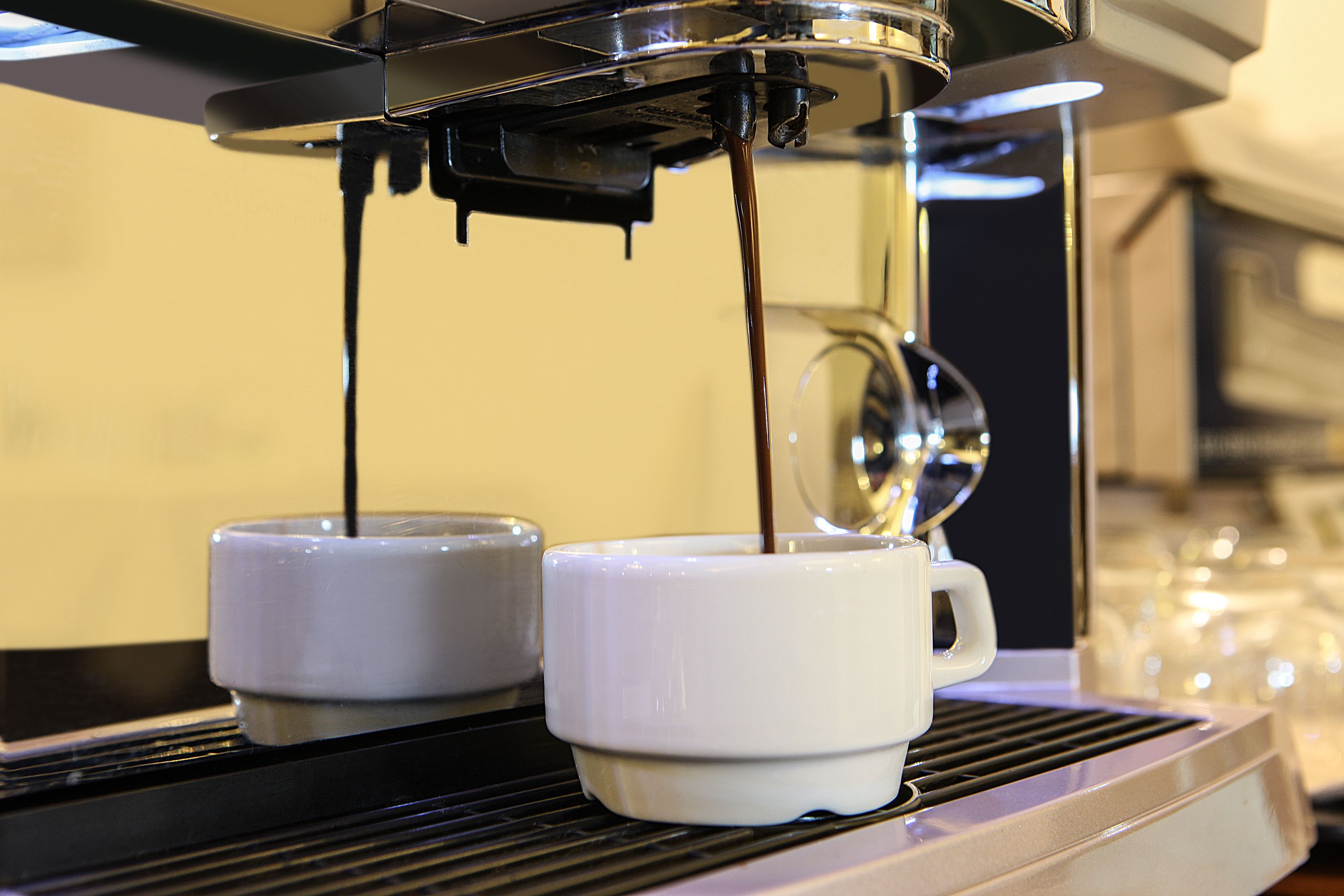 A coffee machine dispensing espresso into two white cups.