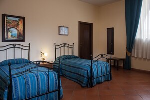 Una stanza con due letti, una porta, un tavolino e un quadro appeso al muro.
