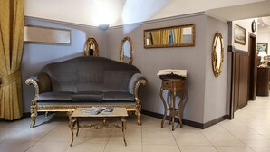A living room with a dark grey sofa, ornate gold-framed mirrors, and a small wooden side table with a book. - Grand Hotel Capodimonte (Naples)