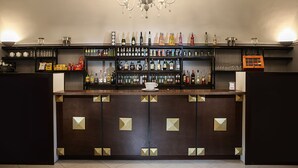 A bar area with a dark wood counter, shelves with bottles, glasses, and a chandelier. - Grand Hotel Capodimonte (Naples)