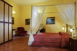 A bedroom with a four-poster bed, a red chair, and two wall-mounted lamps.
