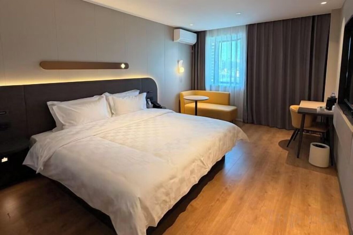 Une chambre d’hôtel avec un grand lit, une petite table, une chaise et une fenêtre avec des rideaux.