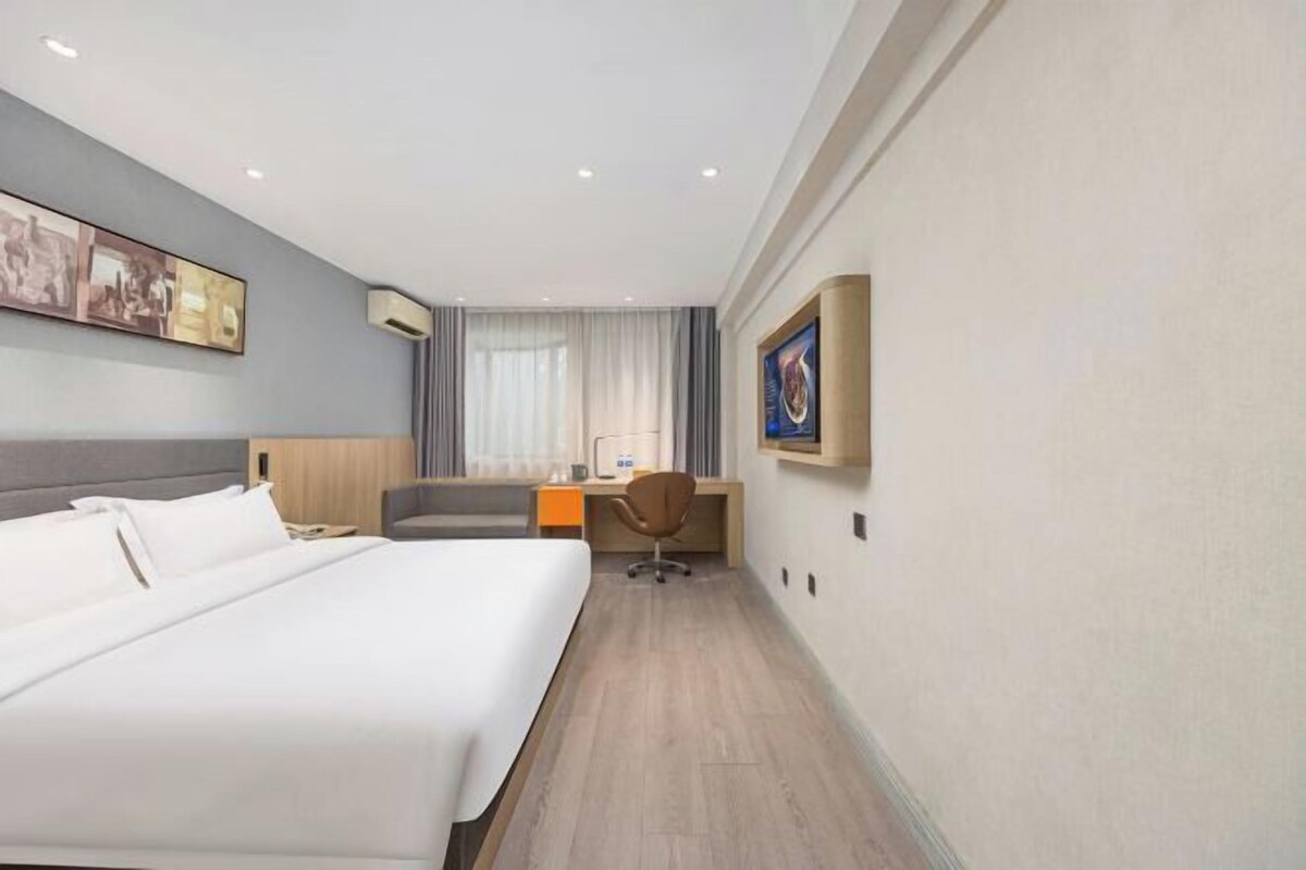 Een hotelkamer met een groot bed, een bureau, een stoel en een raam met gordijnen.