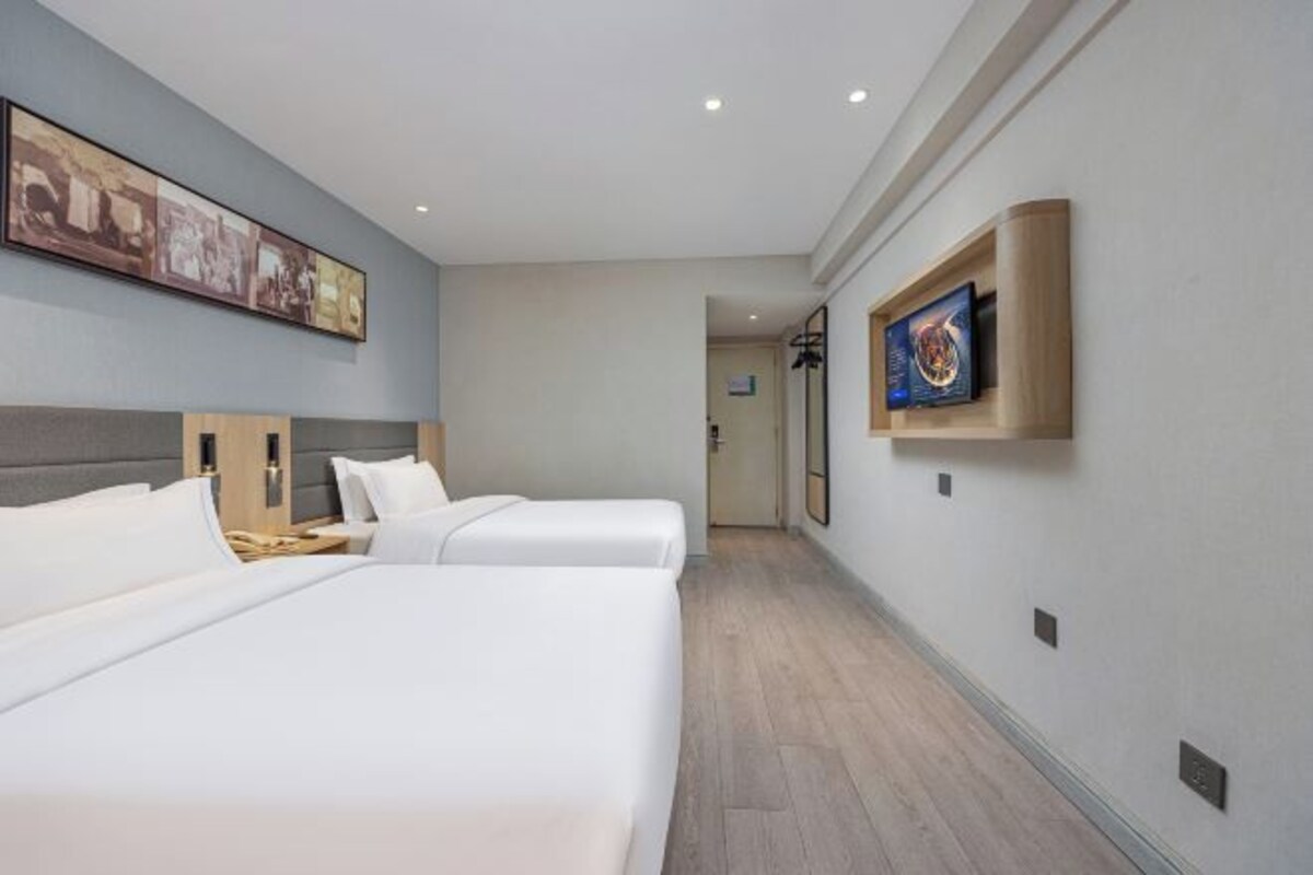 A hotel room with two beds, a large framed picture on the wall, and a small TV mounted on the wall.