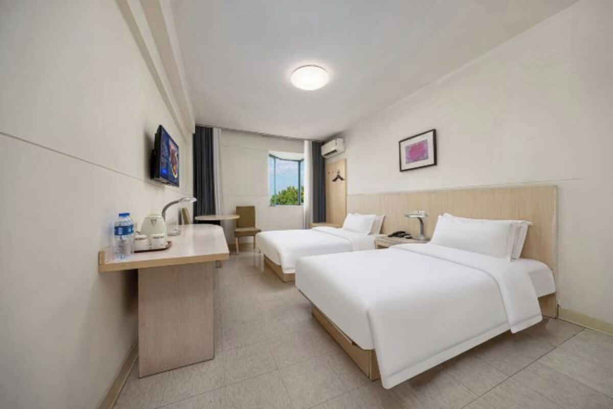 A hotel room with two beds, a desk, a chair, a TV, and a window.