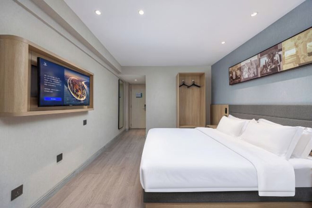 A modern hotel room with a large bed, a mounted TV, and a wardrobe.