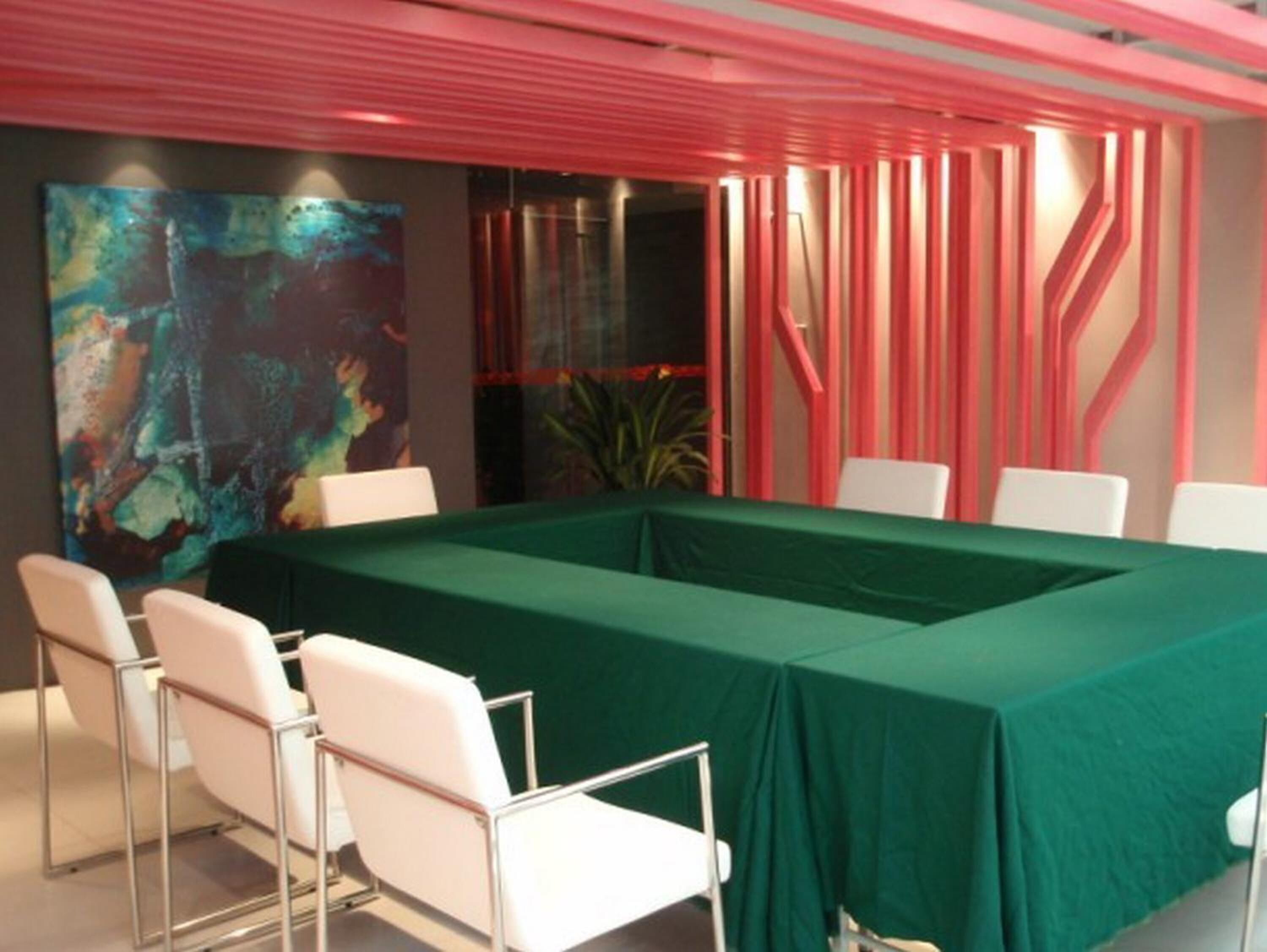 Un salón de conferencias con una mesa verde, sillas blancas y arte abstracto en la pared.
