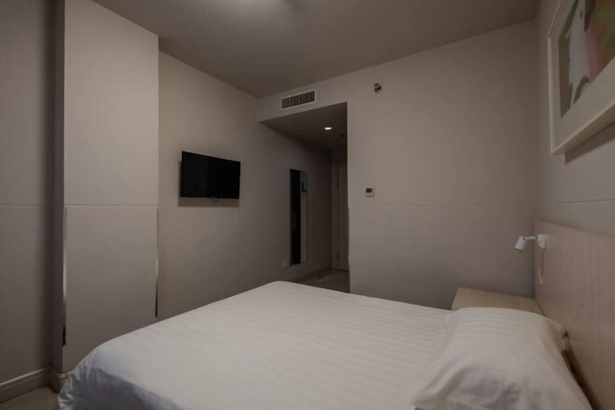 A bedroom with a bed, a flat-screen TV mounted on the wall, and a door leading to another room.