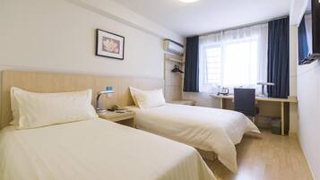 A hotel room with two beds, a desk, a chair, a lamp, a picture on the wall, and a window with curtains.
