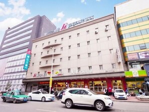 A multi-story hotel with a prominent signage, a street view with cars, and a clear sky. - Jinjiang Inn (Shenyang Middle Street Metro Station, Imperial Palace) (Shenyang)