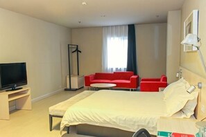 A hotel room with a bed, a TV, a red sofa, a small table, and a standing lamp. - Jinjiang Inn (Shenyang Middle Street Metro Station, Imperial Palace) (Shenyang)
