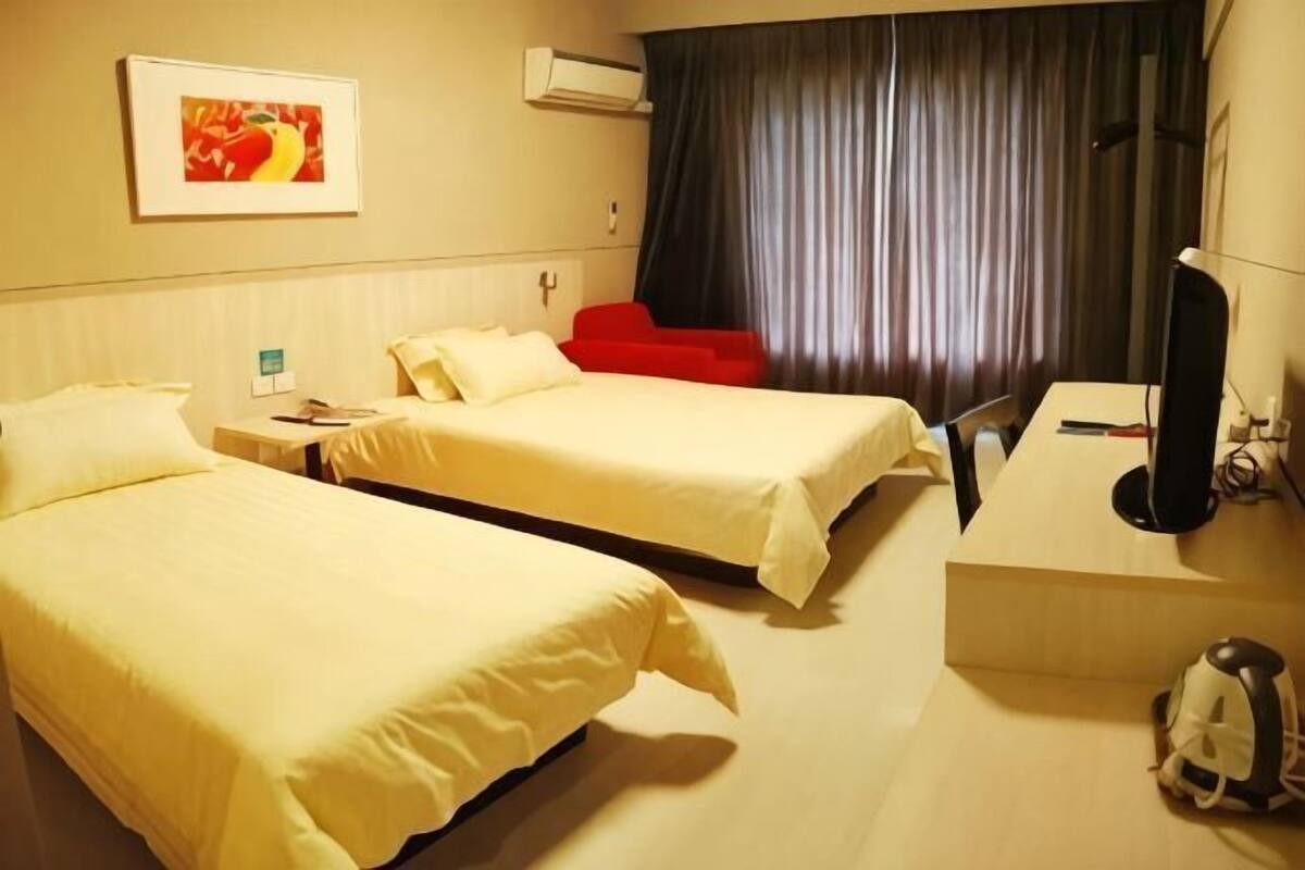 A hotel room with two beds, a desk, a chair, a television, and a window with curtains.