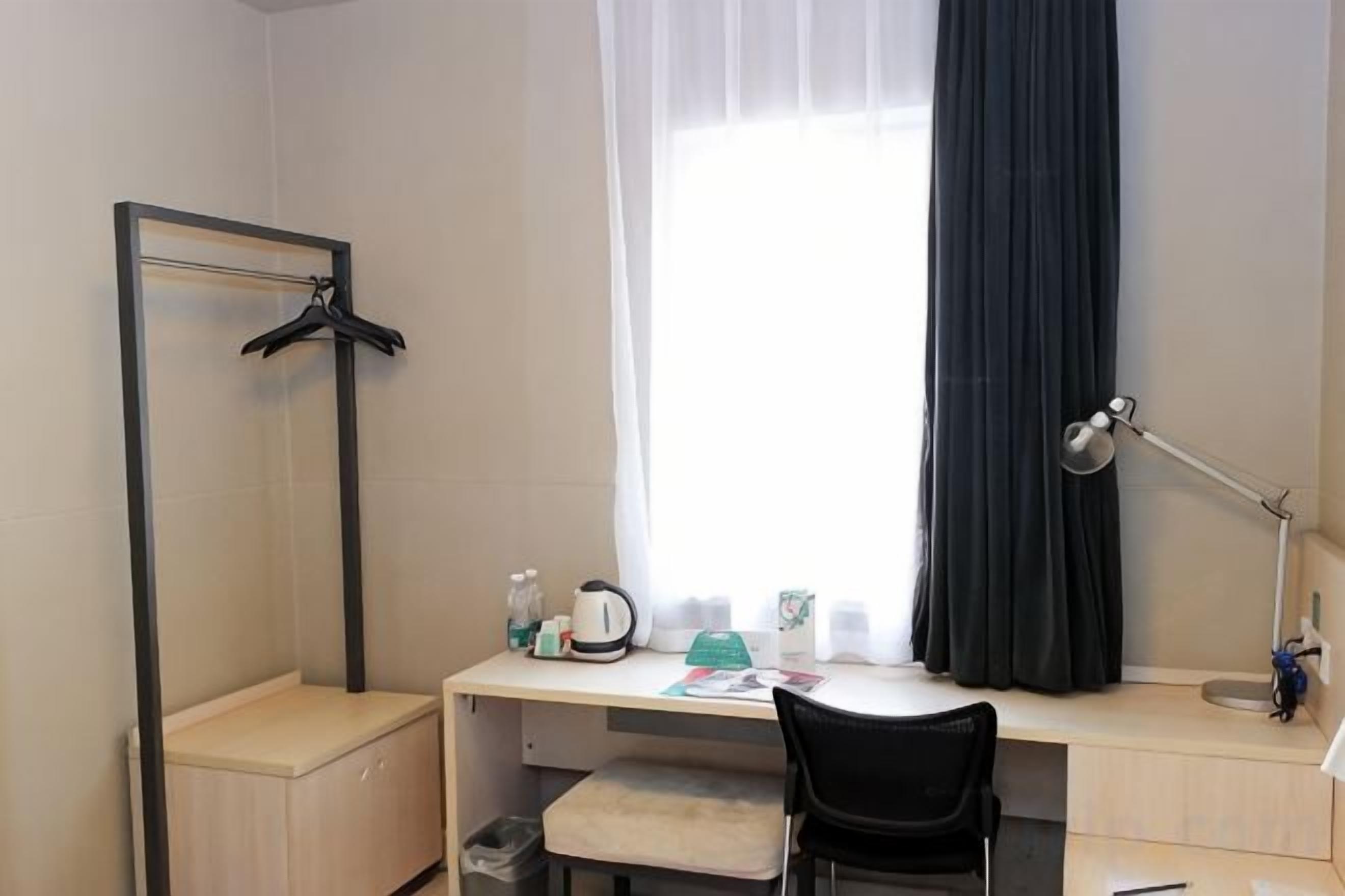 A hotel room with a desk, chair, and a mirror.