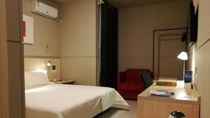 A hotel room with a bed, a desk with a lamp, a red chair, a coffee maker, and a mirror. - Jinjiang Inn Chongqing Shopping & Entertainment (Chongqing)