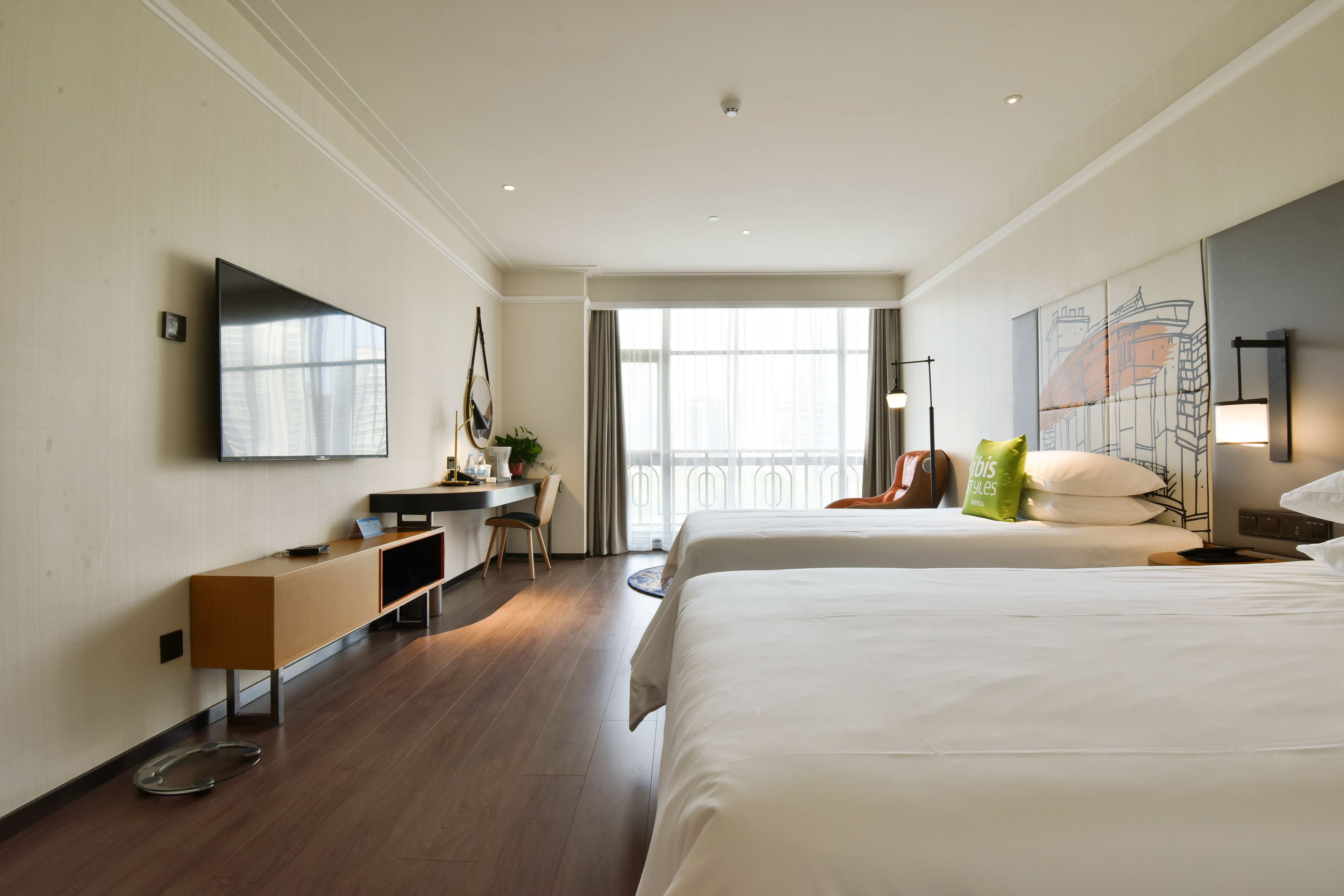 Habitación de hotel con una cama grande, un escritorio con silla, un televisor en la pared y una ventana con cortinas.