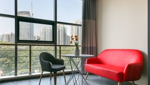 A modern room with a large window, a red sofa, a black chair, and a small table with a vase of flowers.