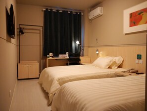 Une chambre d’hôtel avec deux lits, un bureau, une chaise, une lampe de bureau, un climatiseur et un tableau au mur.