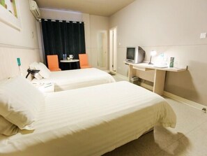 Une chambre d’hôtel avec deux lits, un bureau équipé d’un ordinateur et d’une lampe, une télévision et une petite table avec une tasse et une bouteille.
