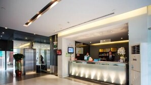 Ein moderner Hotel-Empfangsbereich mit Glastrennwand, Empfangstresen und einem digitalen Bildschirm.