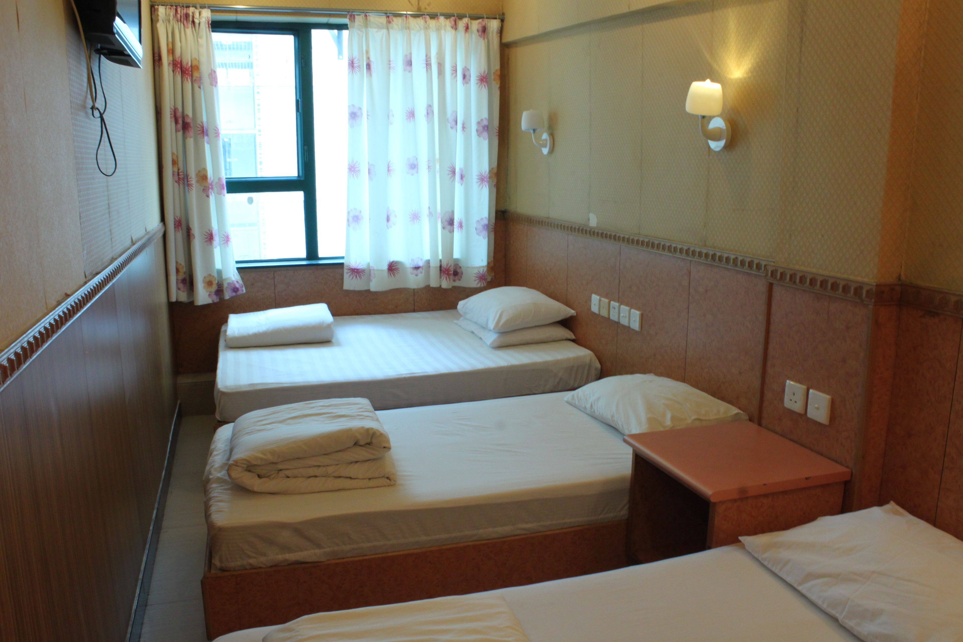 Une chambre d’hôtel avec deux lits simples, une petite table et une fenêtre avec des rideaux.