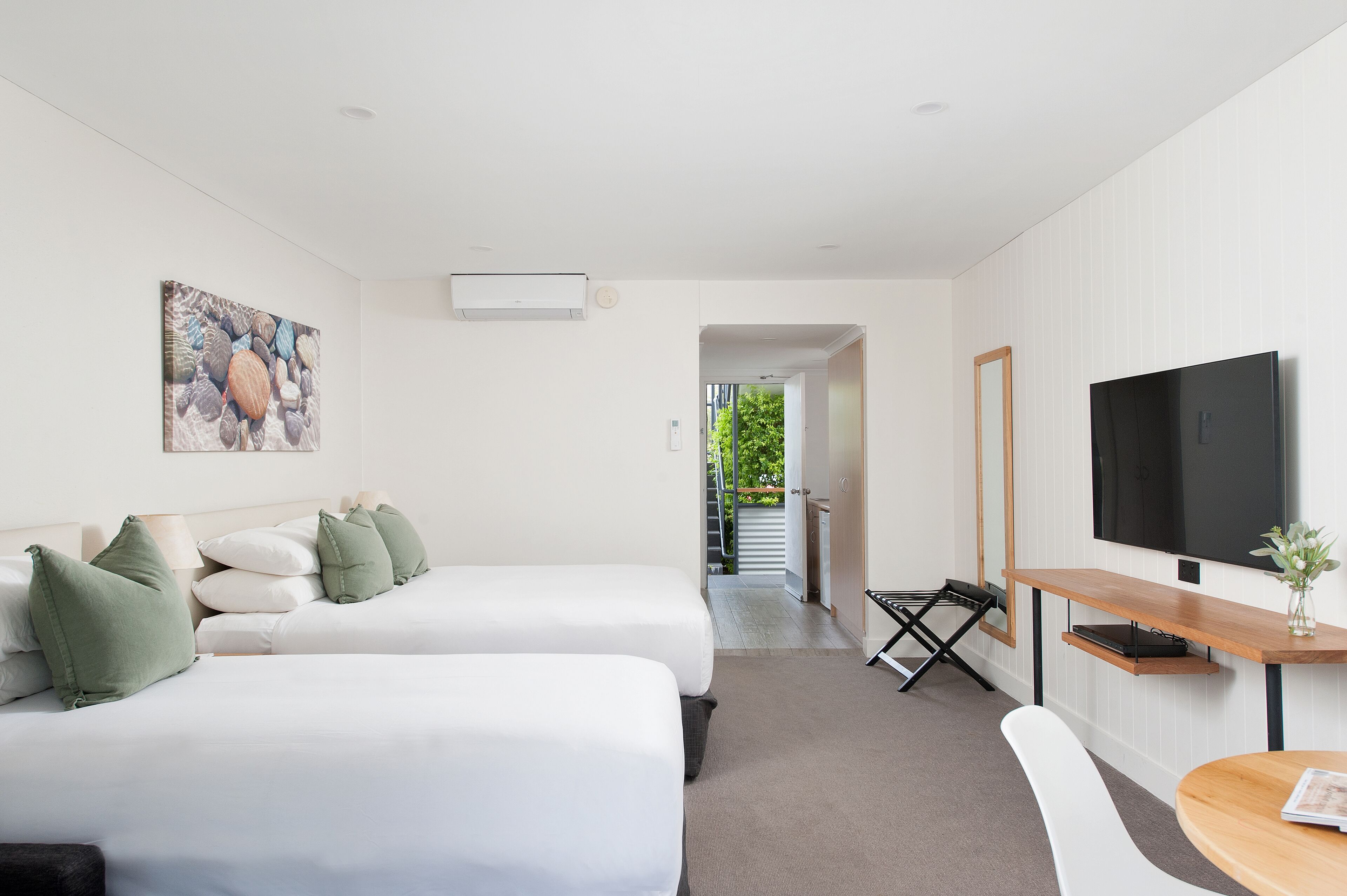 A modern hotel room with two beds, a TV, and a desk.