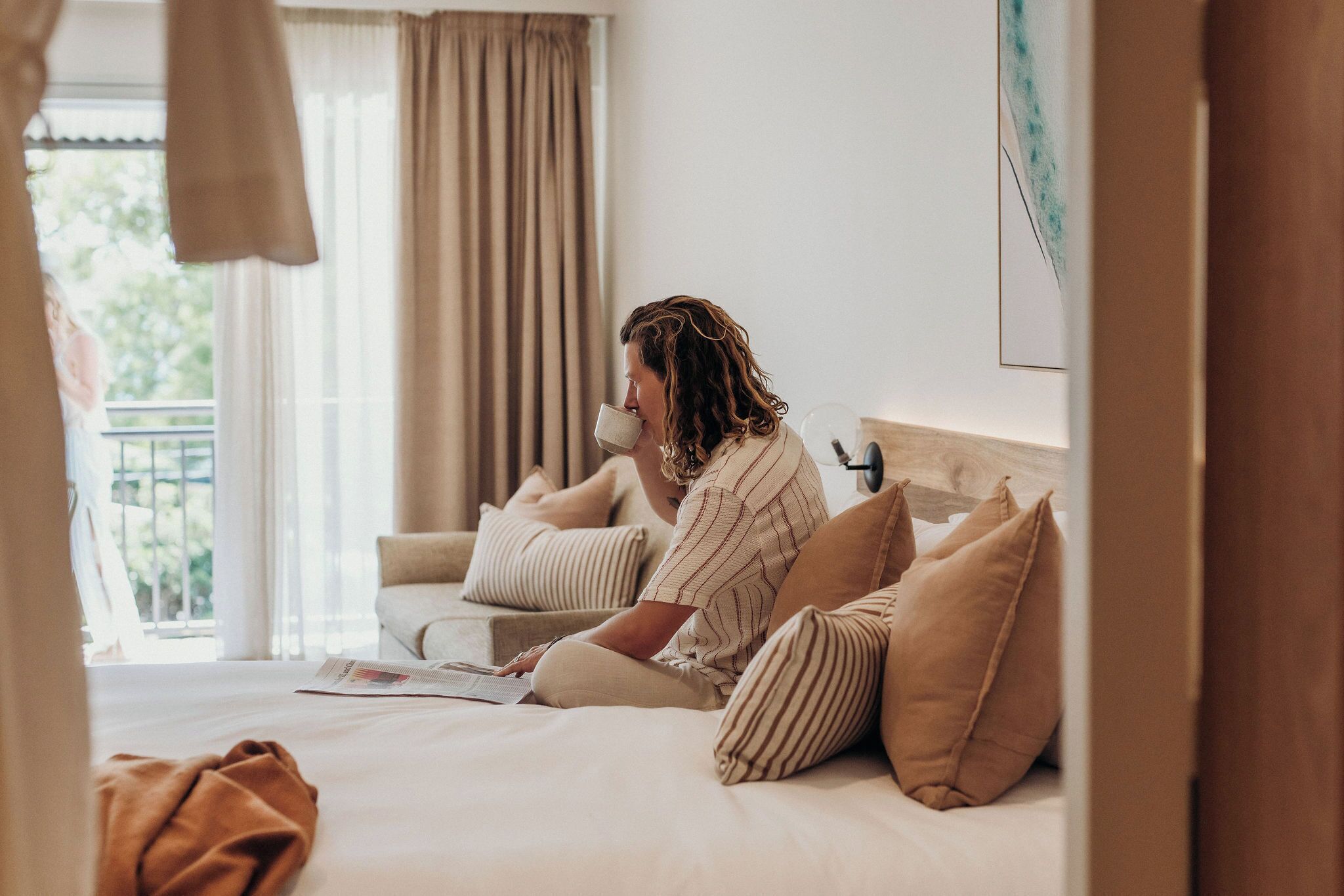 A room with a bed, a window with curtains, a sofa, and a painting on the wall.