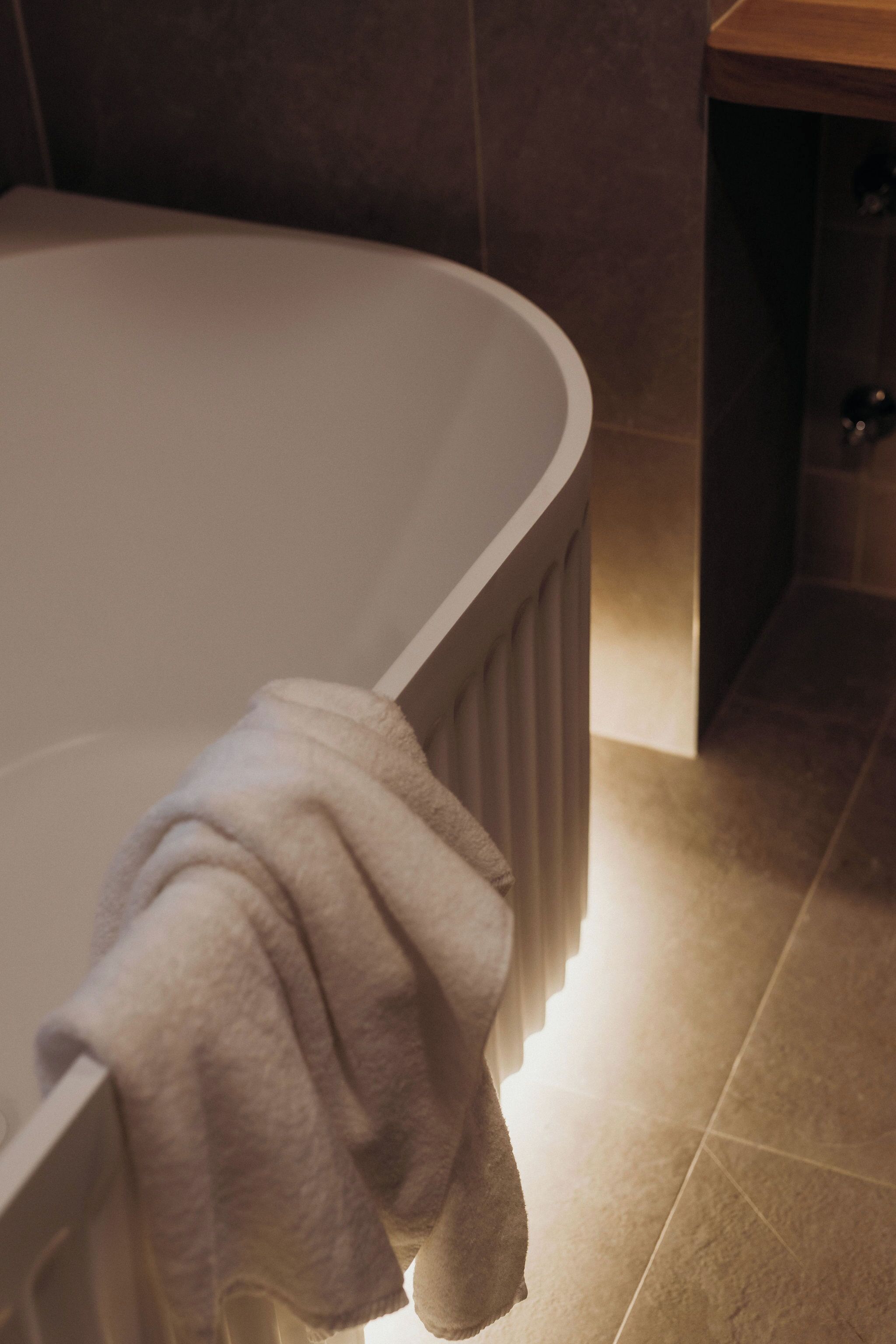 A bathroom with a bathtub, a towel on the edge, and a wooden cabinet.