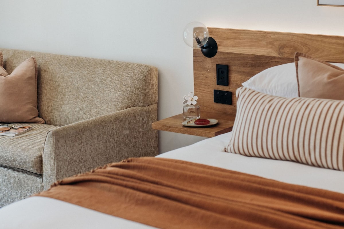 Et hotelværelse med seng, træsengegavl, et natbord, lampe og sofa.