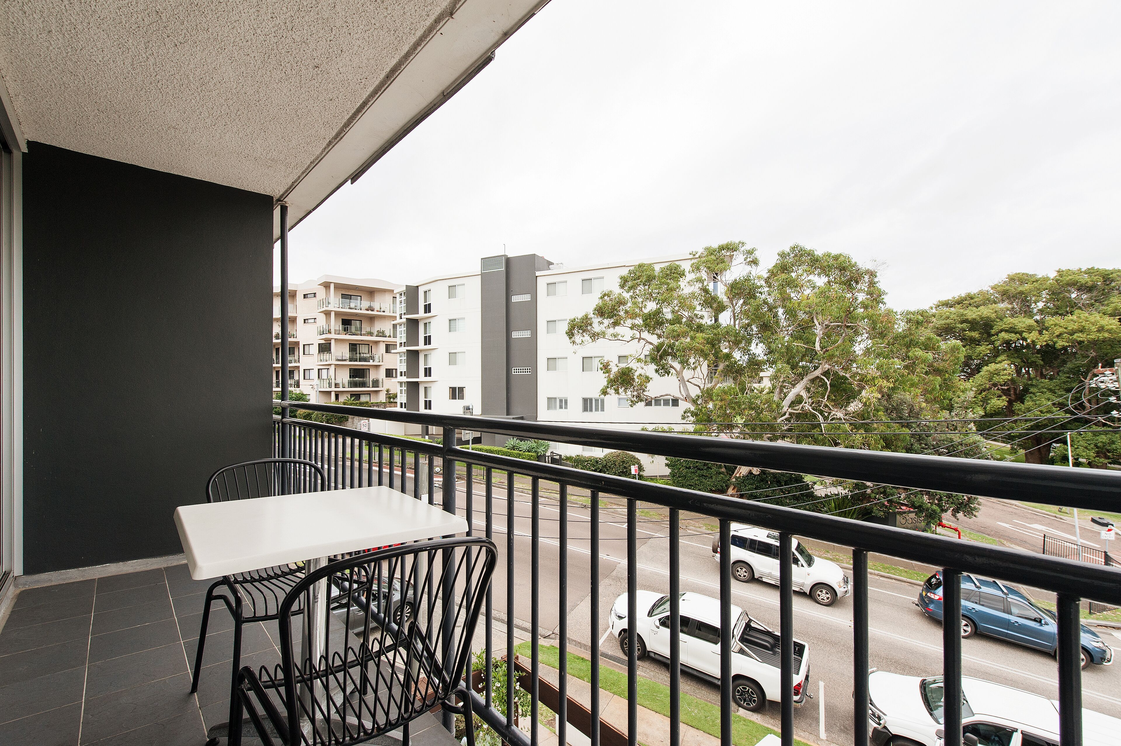 A balcony with a table and chairs, overlooking a street with cars and buildings.