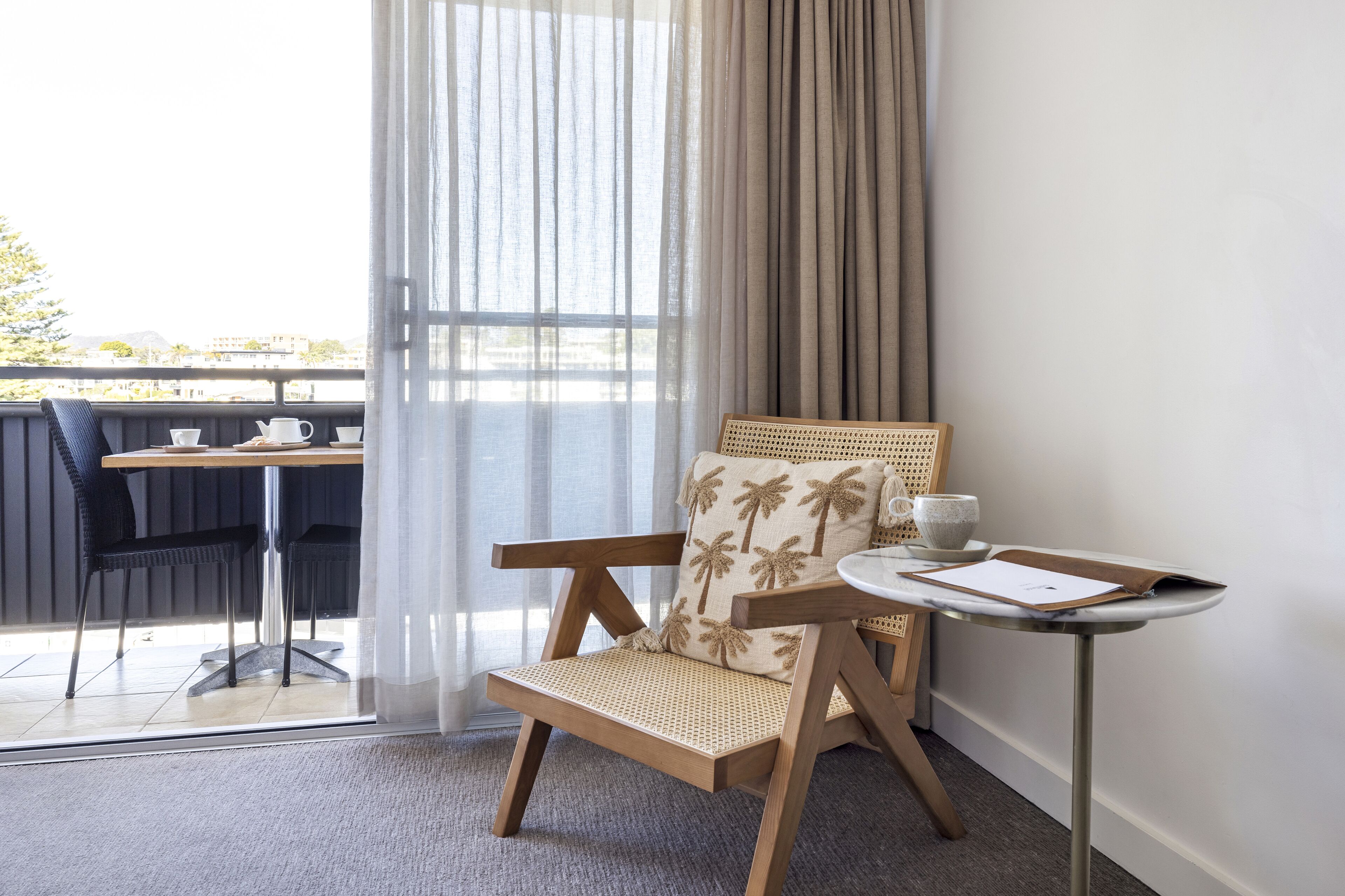 Un balcon avec un fauteuil en osier, une petite table ronde et deux chaises.