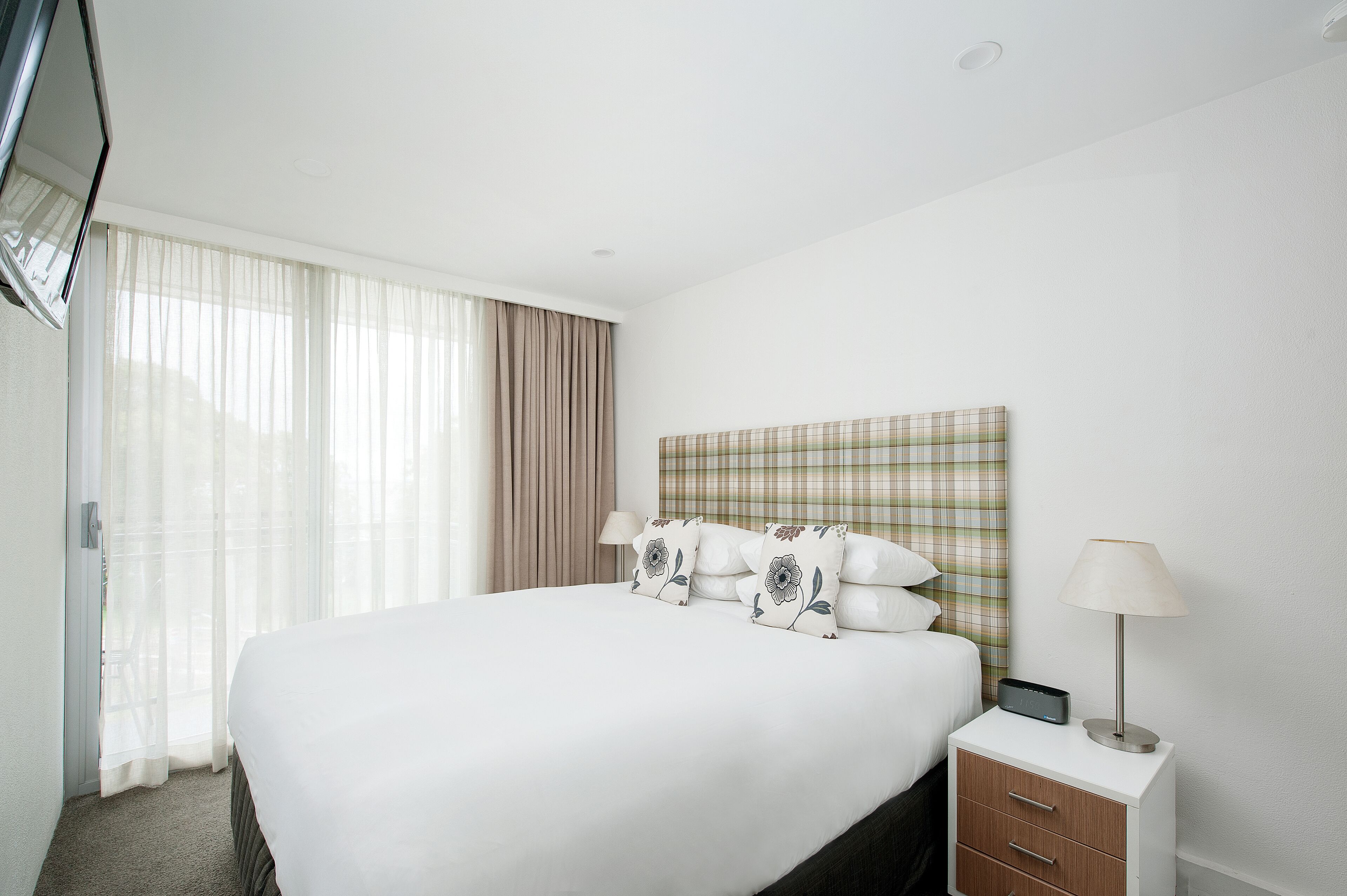 Habitación de hotel con una cama grande, una mesita de noche con lámpara y un cabecero a cuadros.