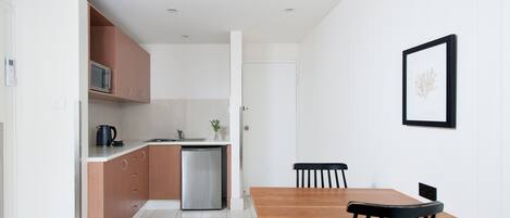 A modern kitchen with a microwave, kettle, and dishwasher, a wooden dining table with chairs, and a framed picture on the wall.