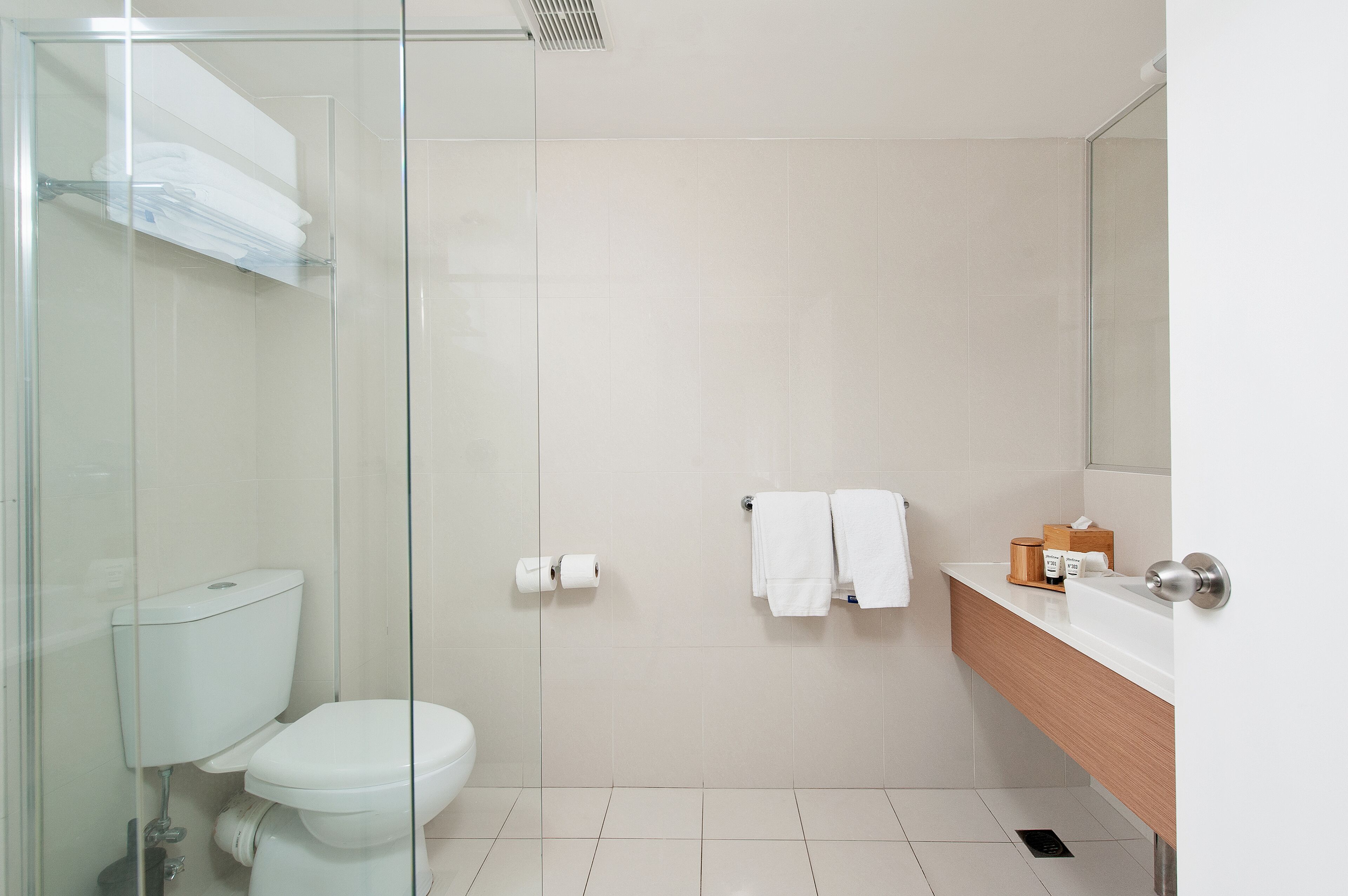 Un baño moderno con cabina de ducha de vidrio, inodoro, lavamanos con espejo y un perchero para toallas.