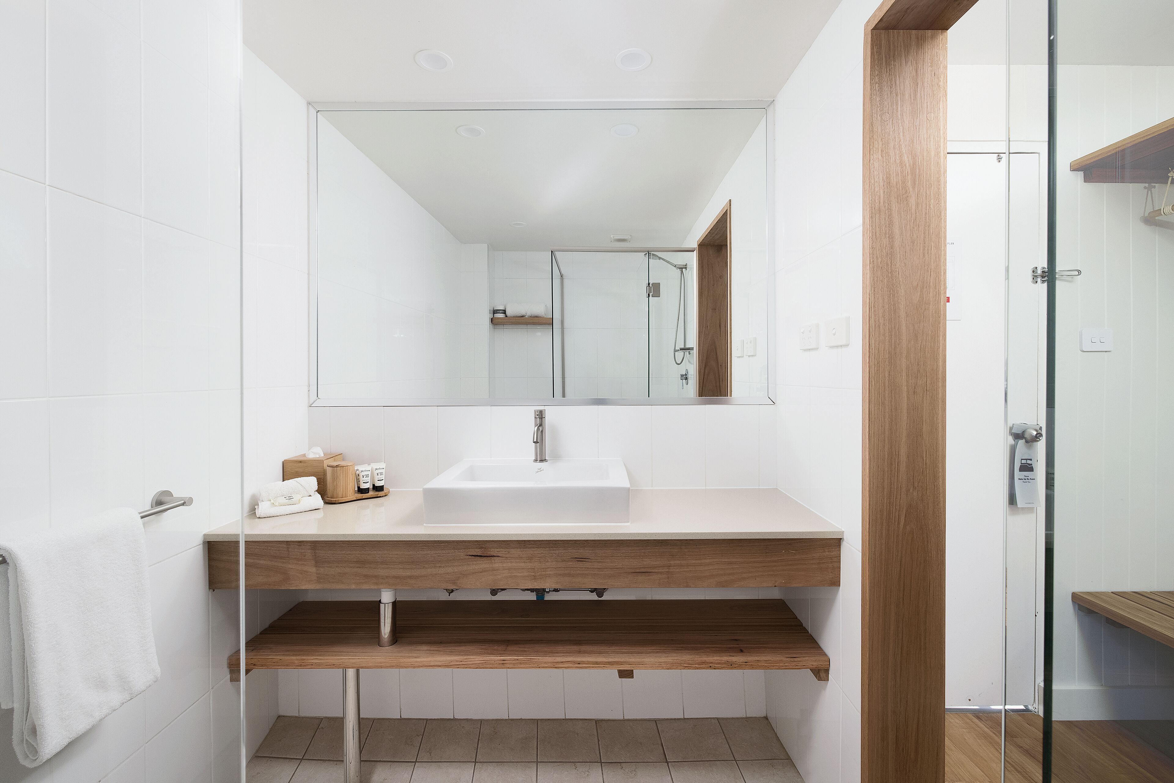 A modern bathroom with a white sink, wooden vanity, and a glass shower enclosure.