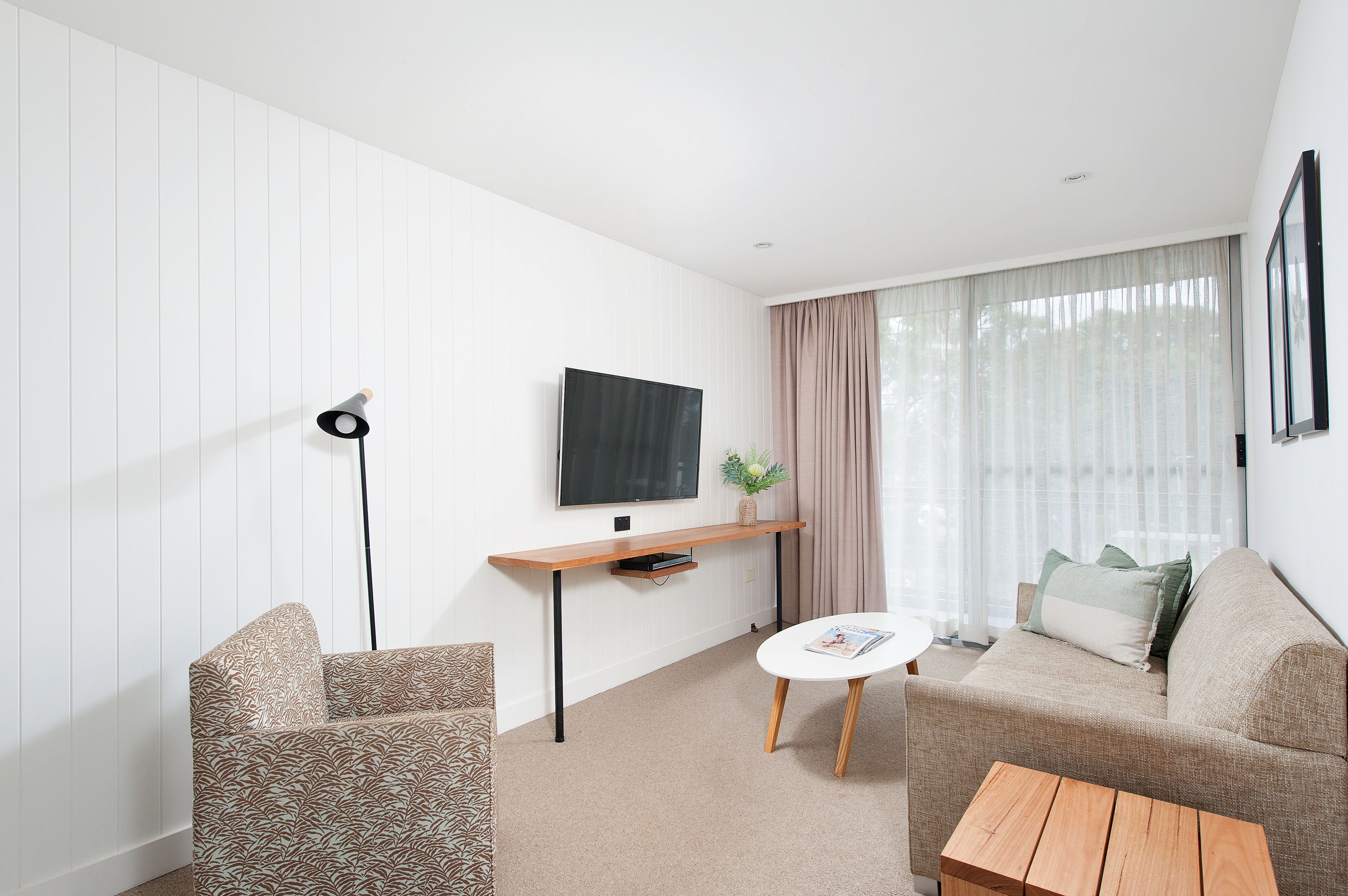 Ein modernes Wohnzimmer mit einer Couch, einem Couchtisch, einem an der Wand montierten Fernseher und einer Stehlampe.