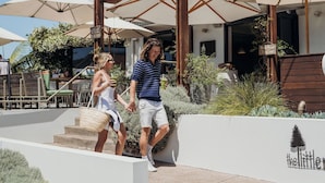 A couple walking outside a restaurant with outdoor seating, wooden pergolas, and a sign that reads "The Little." - Hotel Nelson (Nelson Bay)
