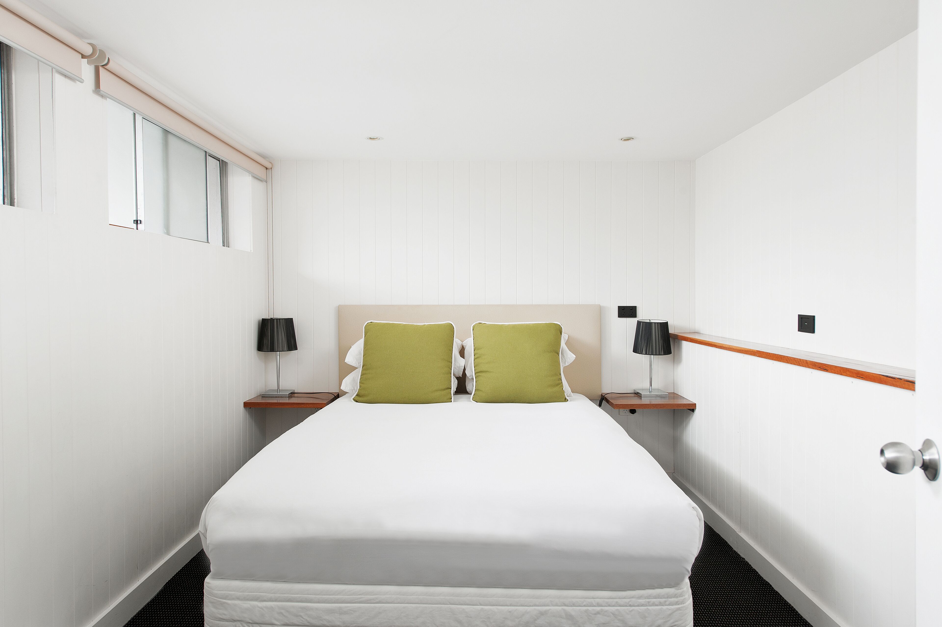 Habitación de hotel con una cama grande, dos mesitas de noche con lámparas y un cabecero de madera.