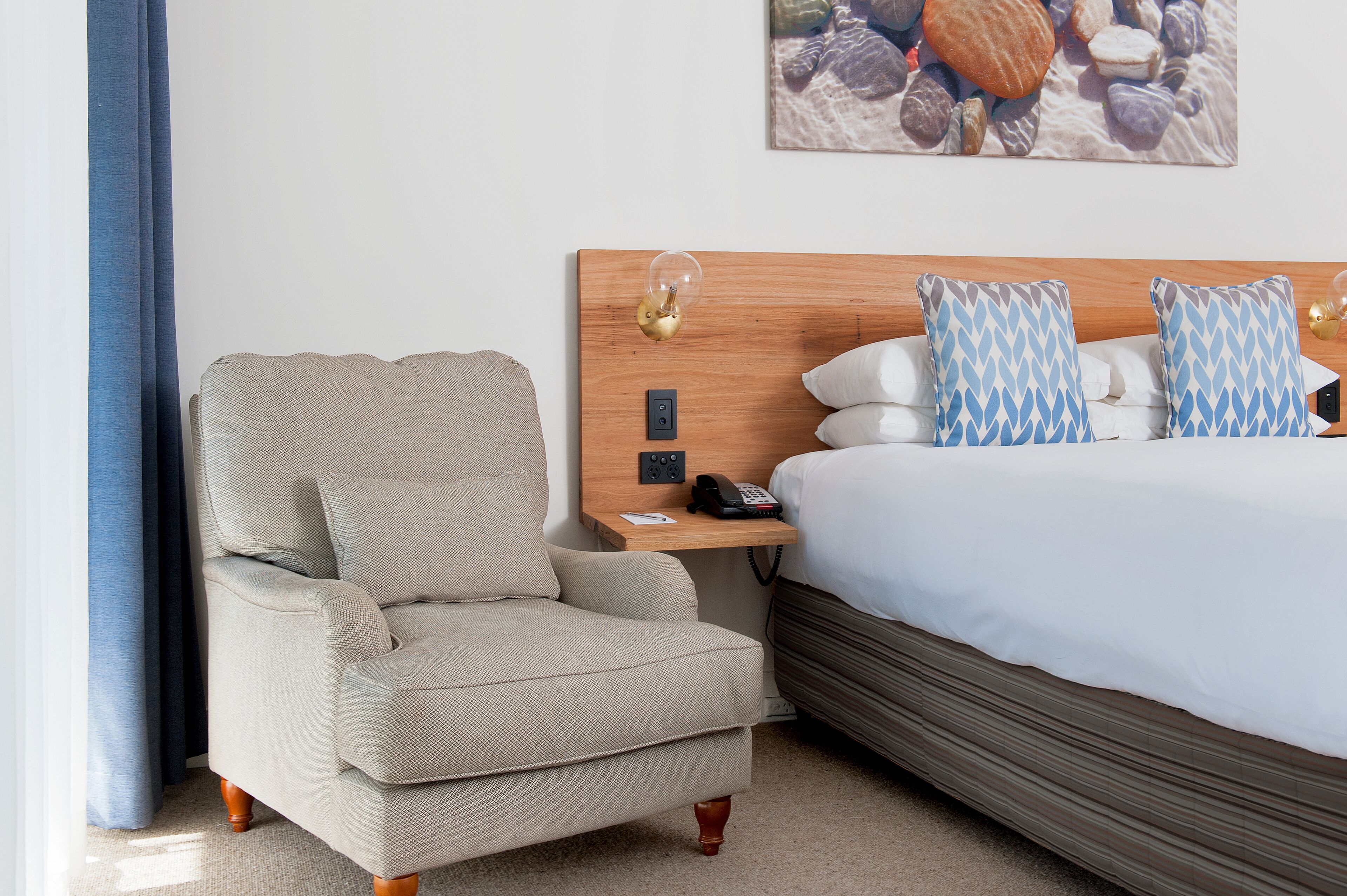 Une chambre d’hôtel équipée d’un lit, d’une chaise, d’une table de chevet et d’un téléphone fixé au mur.