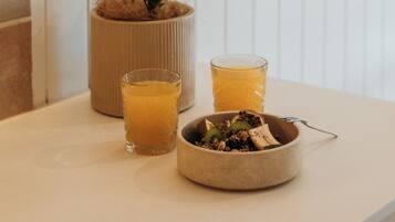 A kitchen counter with a potted plant, two glasses of orange juice, and a bowl of fruit.
