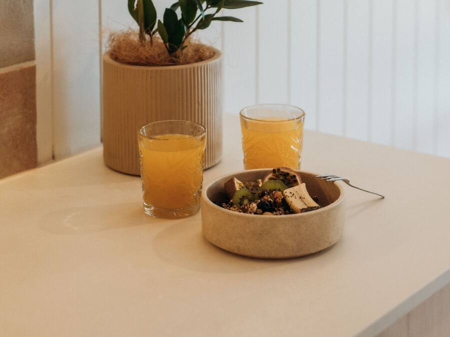 A kitchen counter with a potted plant, two glasses of orange juice, and a bowl of fruit.