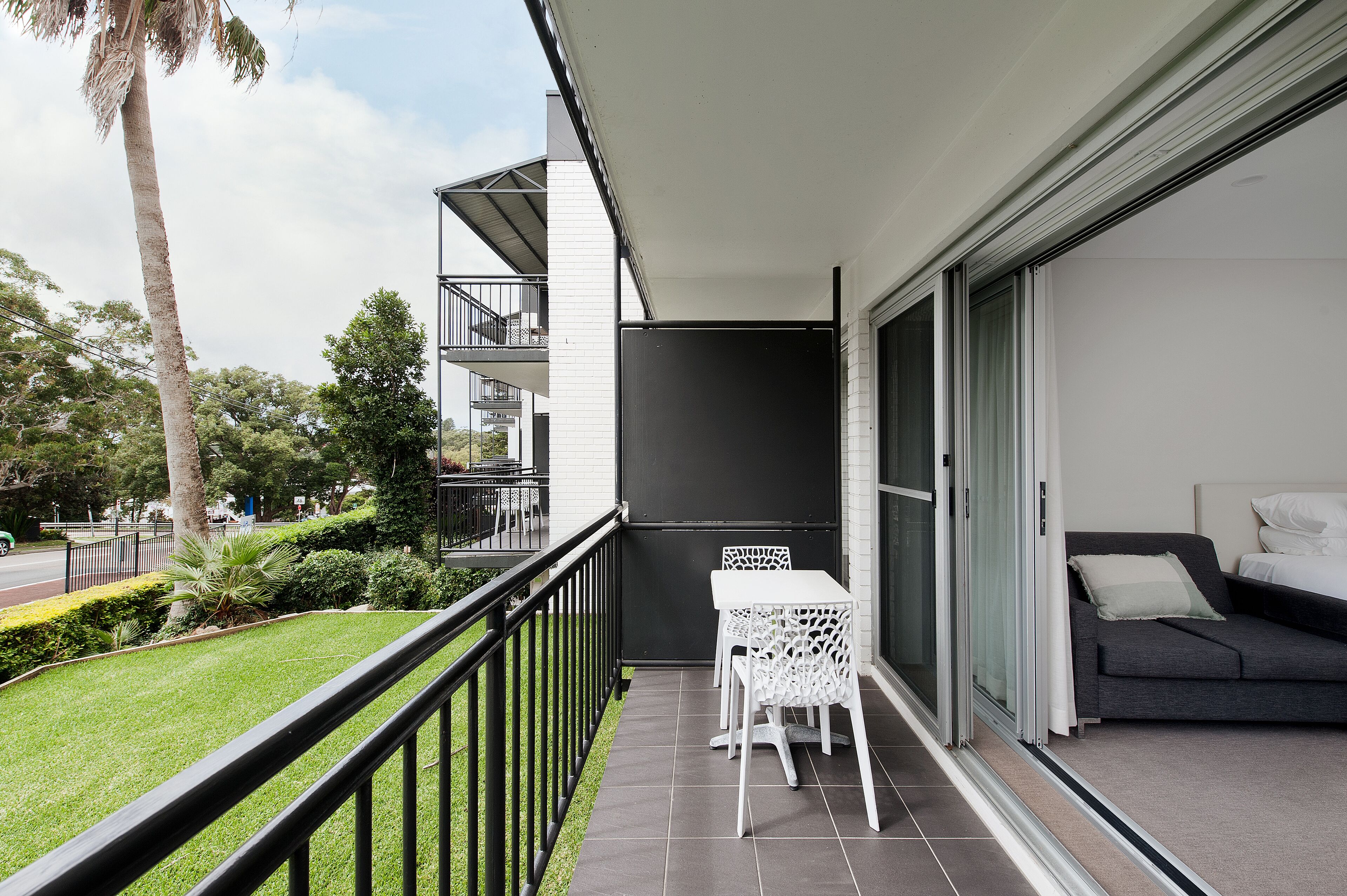 A balcony with a table and chairs, a sofa, and a sliding glass door leading to a bedroom.
