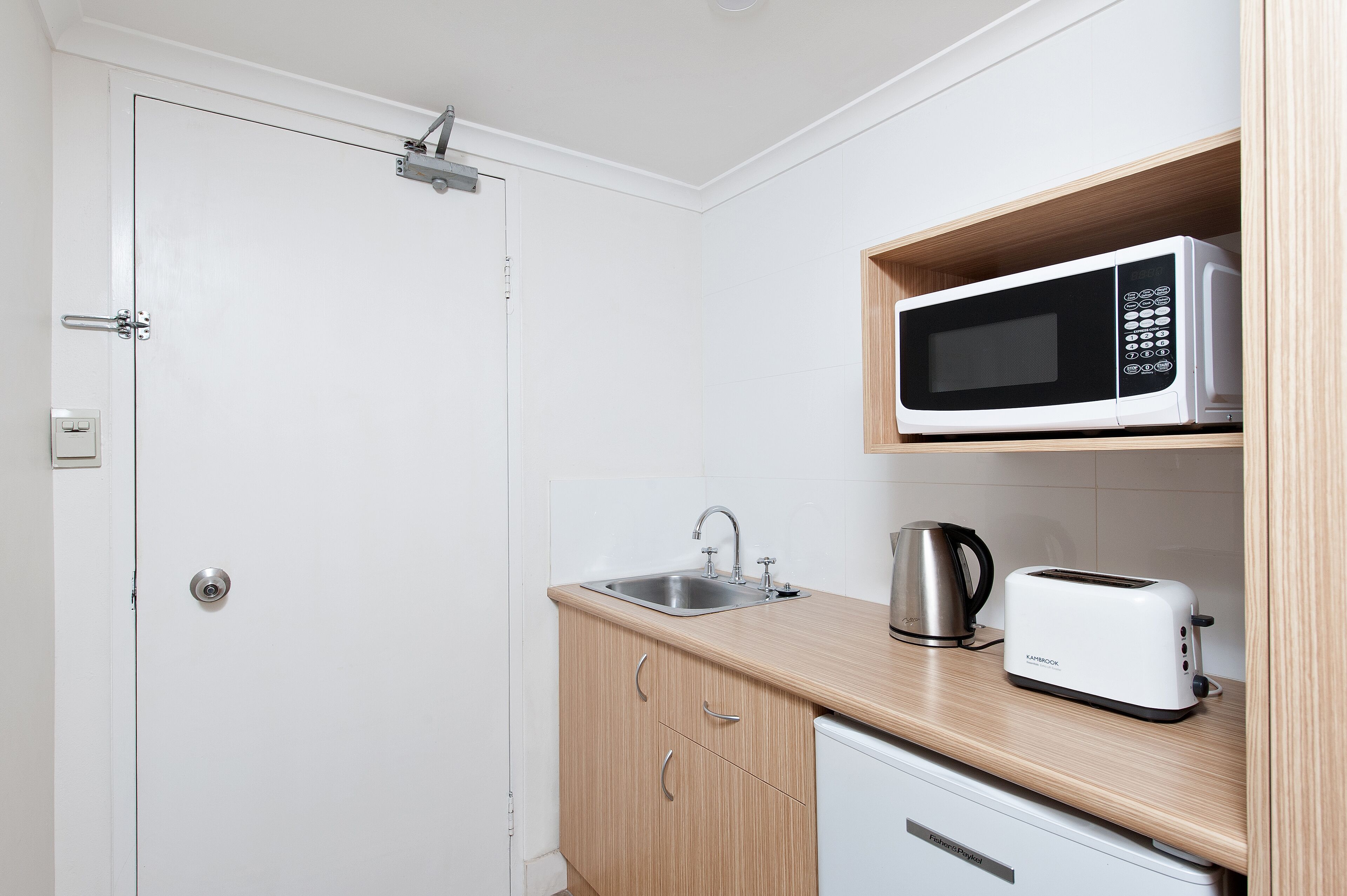 A small kitchenette with a microwave, toaster, and kettle on the countertop.