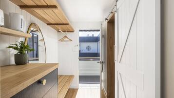 Un couloir étroit avec des étagères en bois, une plante en pot et une vue sur un balcon extérieur.