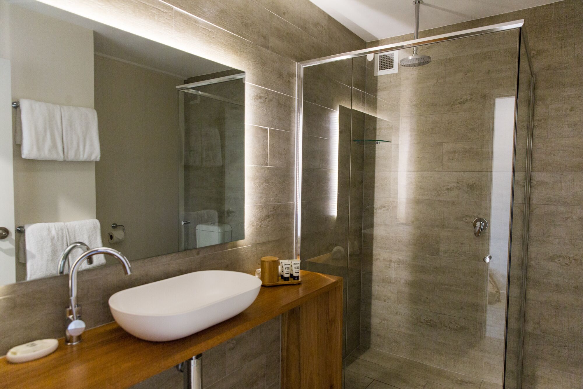 A modern bathroom with a glass-enclosed shower, a wooden vanity with a white sink, and a large mirror.