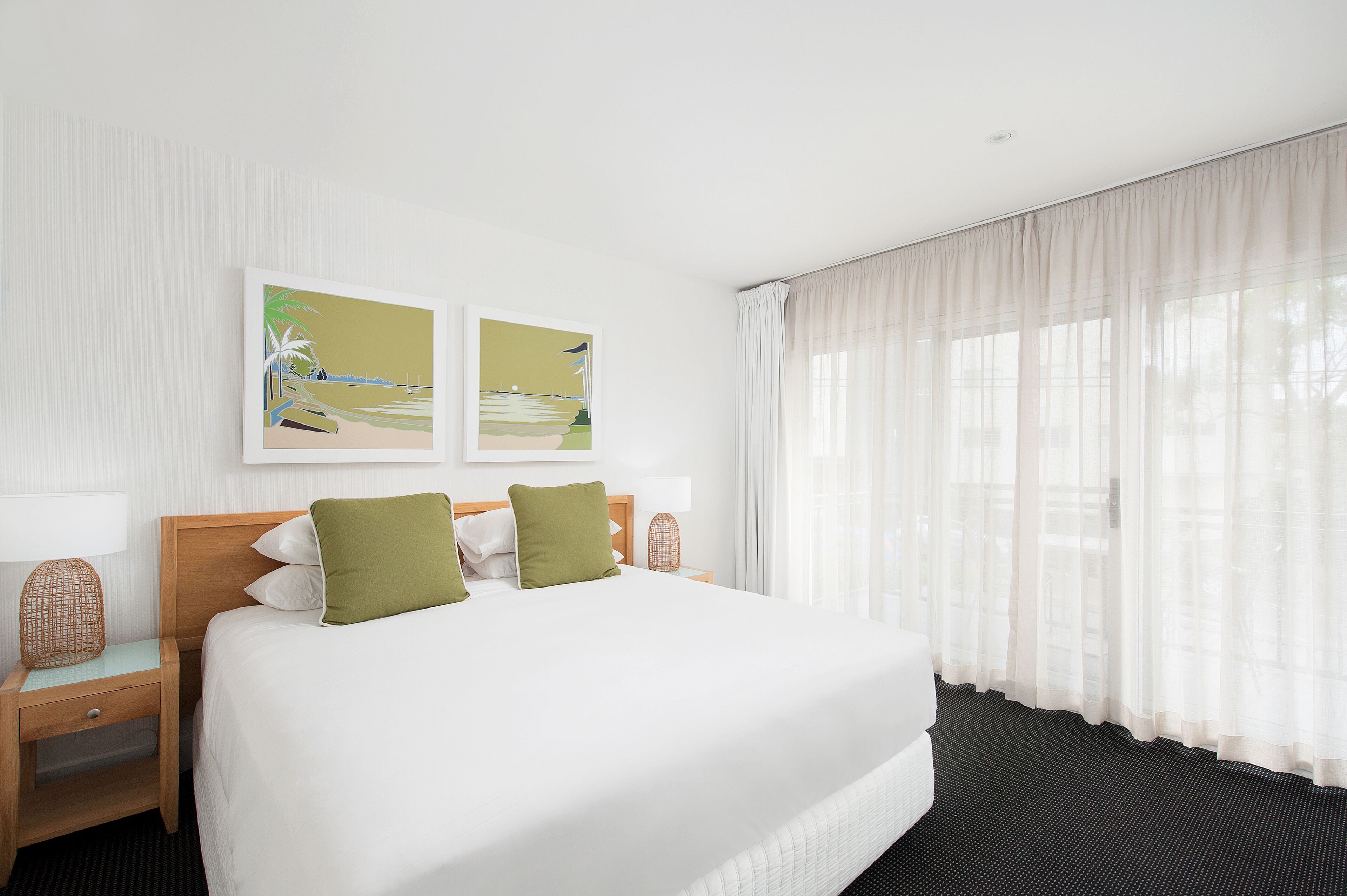 Habitación de hotel con una cama grande, dos almohadas, una mesita de noche, una lámpara y dos obras de arte en la pared.