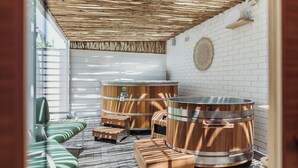 A sauna area with wooden benches and large copper barrels, white brick walls, and a straw ceiling. - Hotel Nelson (Nelson Bay)